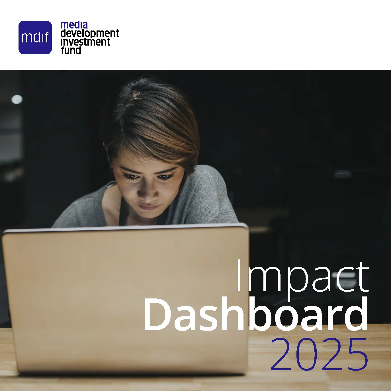 A woman with short brown hair intently looking at a laptop screen in a dimly lit room. The image features the logo of Media Development Investment Fund (MDIF) in the top left corner, with the text “Impact Dashboard 2025” in bold on the lower right.
