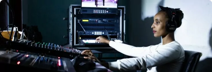 A woman with headphones in a studio controlling the sound.